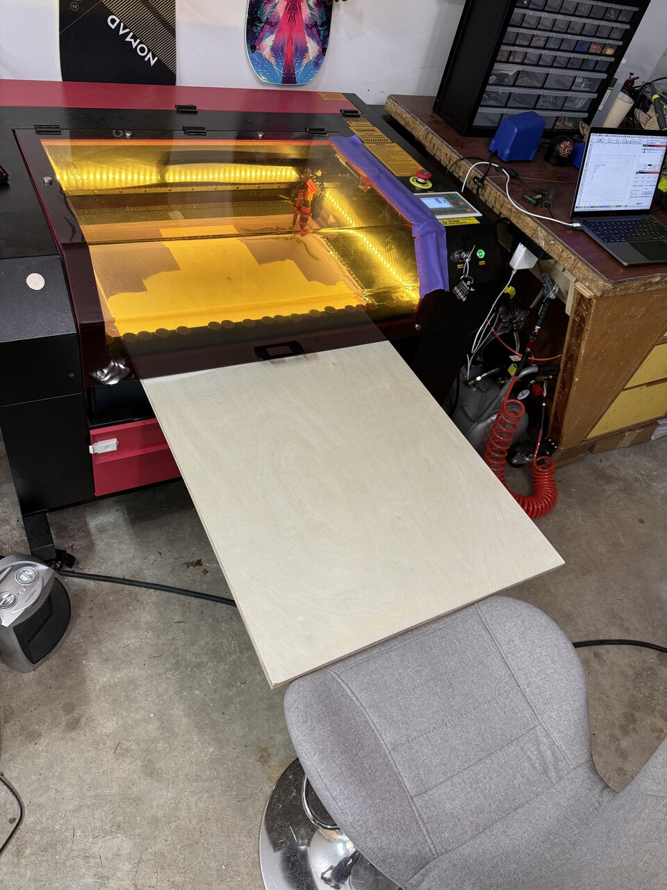 A wooden cornhole board panel extending from the laser engraver.