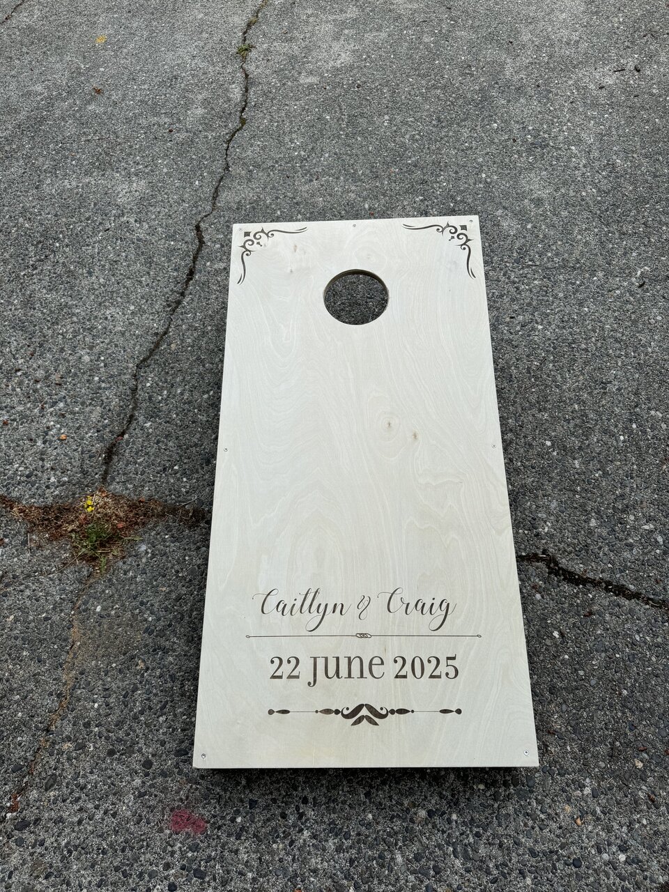 Completed personalized cornhole board with a round opening, resting on the driveway.