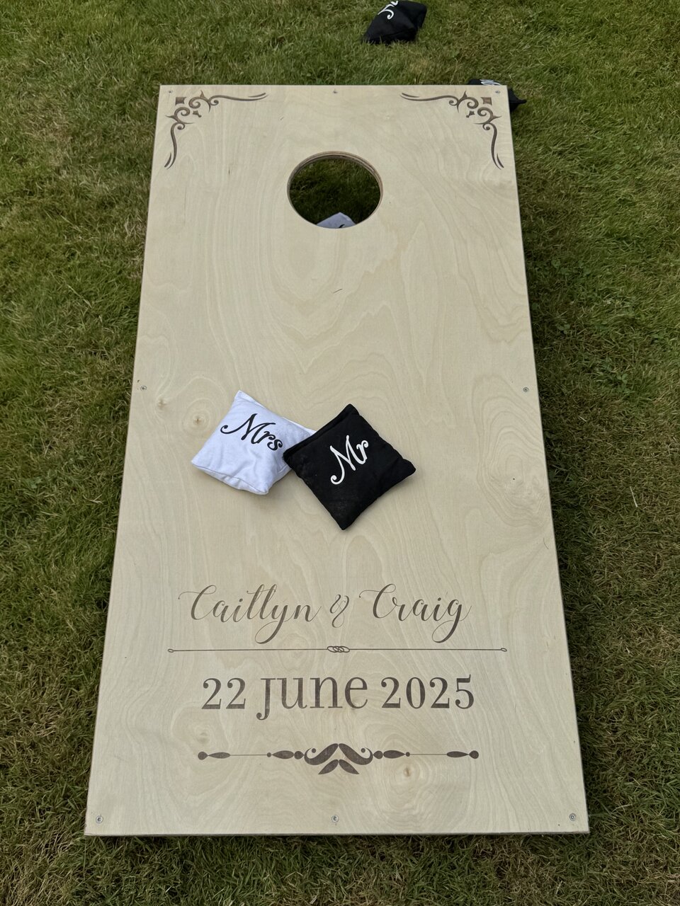 Finished engraved cornhole board on grass with black Mr and white Mrs bean bags.