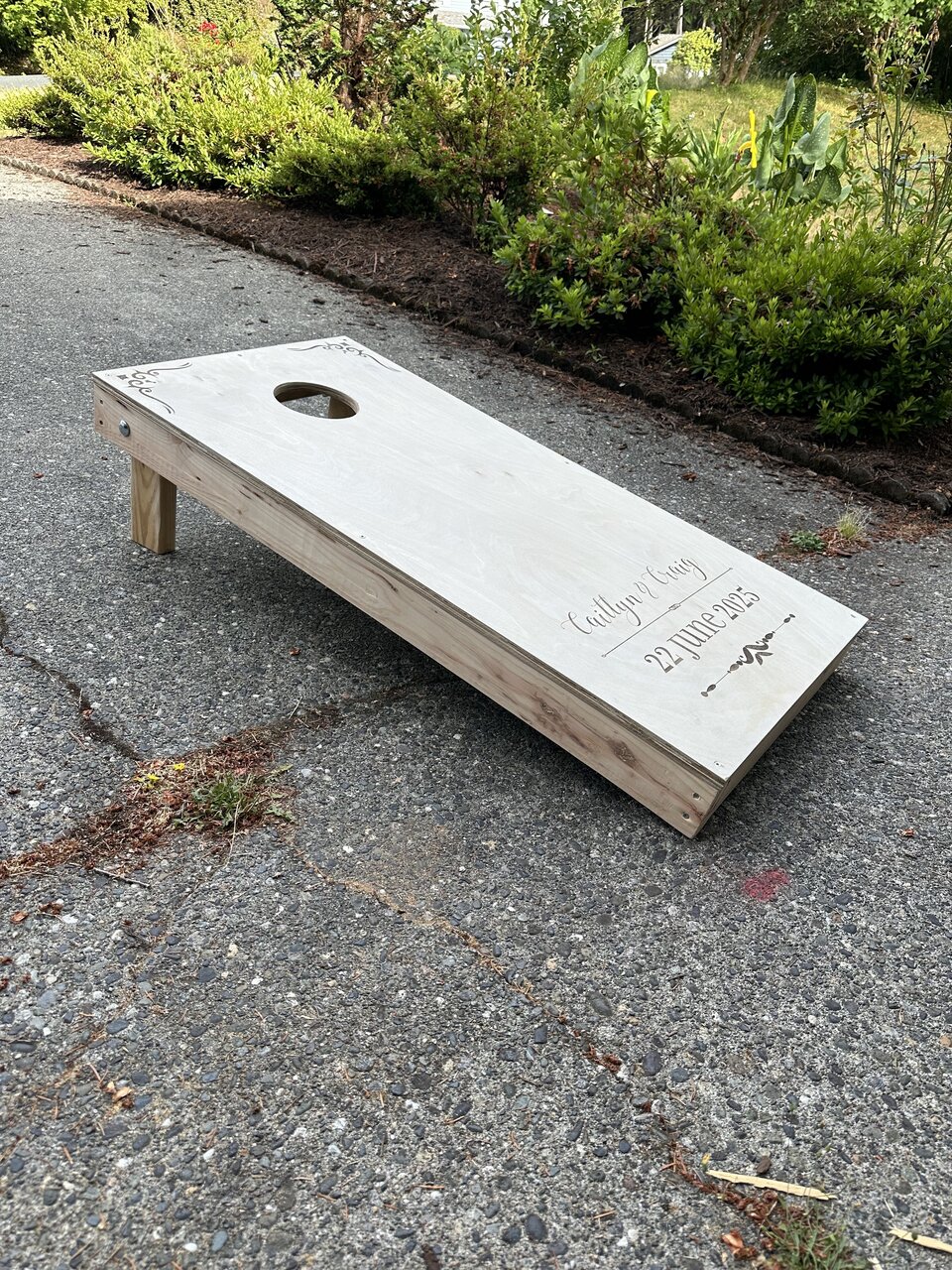 Finished cornhole board set up on its legs outdoors, showing the wooden side frame.